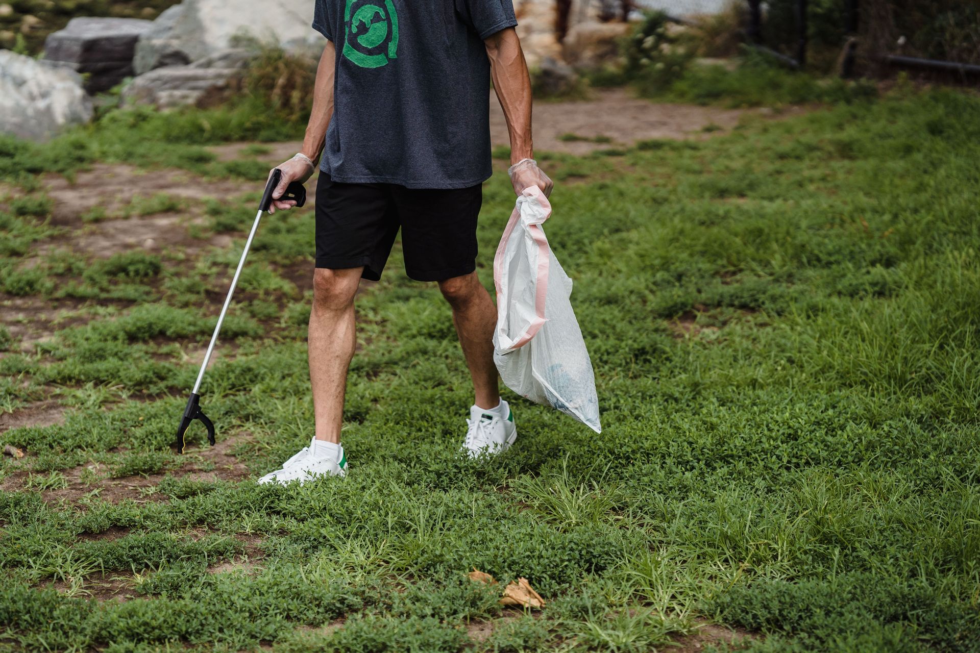 Man picking up litter in a park with gloves and a trash bag, promoting eco-friendly practices.
