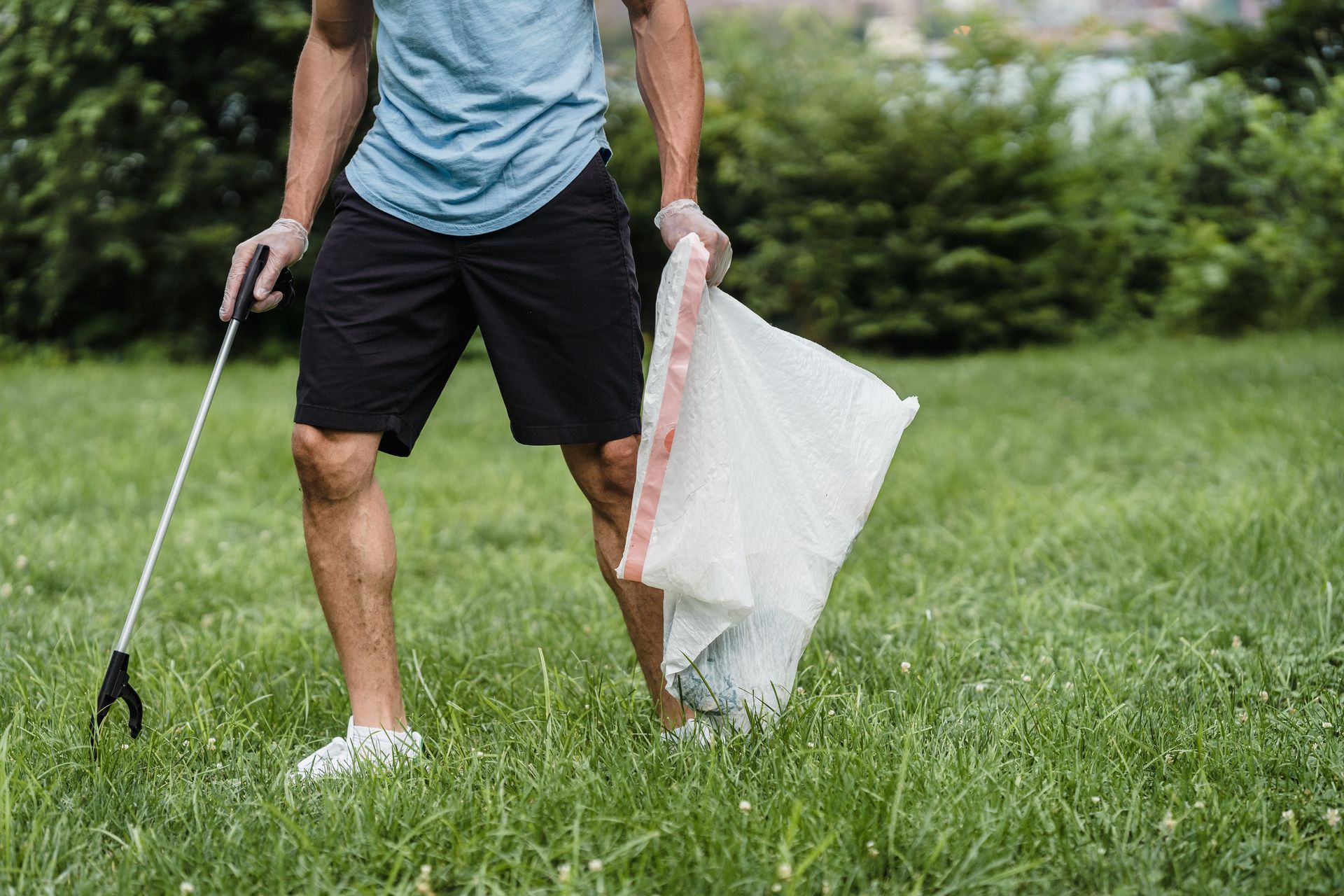 A volunteer cleaning a park, holding a grabber and garbage bag, promoting environmental well-being.